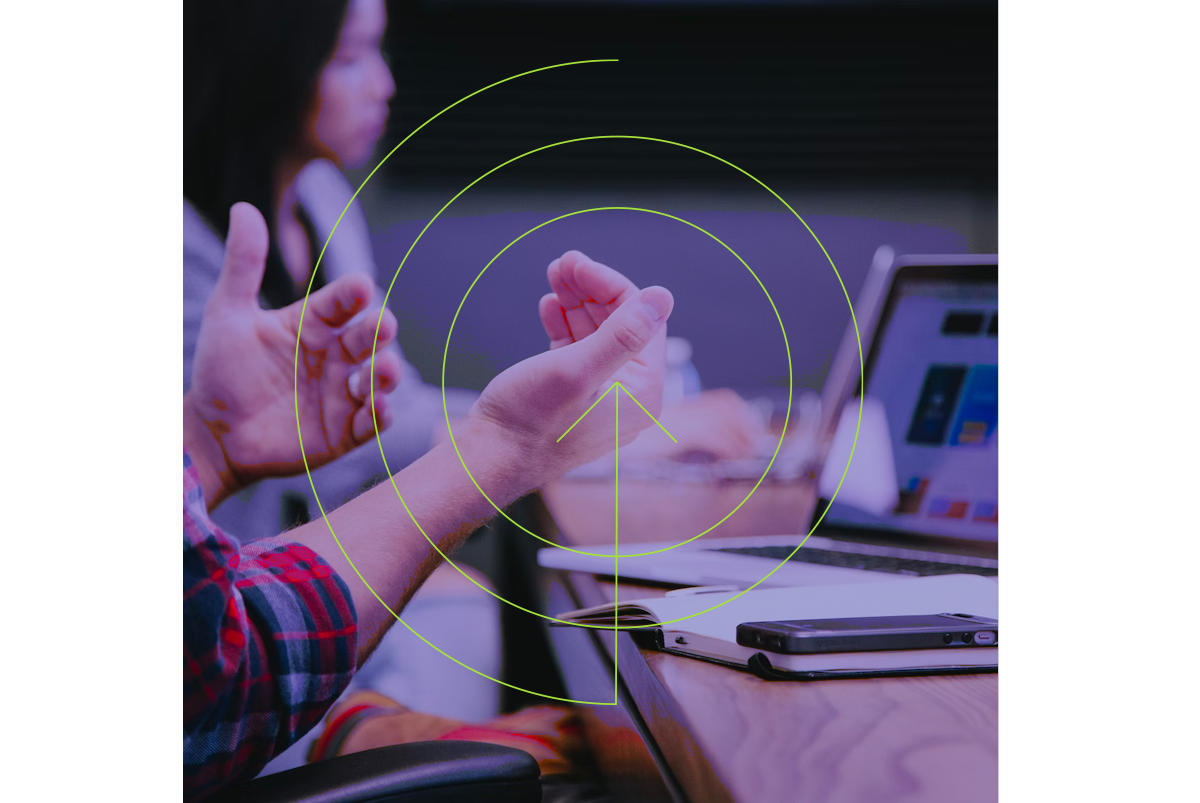 An image showing a person on a laptop in a meeting.